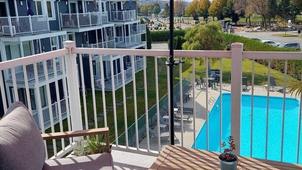 A balcony with a red umbrella, a pool, and a view of a multi-story building. - Central & Cozy Lakeview condo within walking distance of Lake Memphremagog. (Magog)