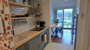 A modern kitchen with a central island, built-in appliances, and a dining area with a view. - Central & Cozy Lakeview condo within walking distance of Lake Memphremagog. (Magog)