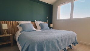 Un dormitorio con cama, cabecera de madera, mesitas de noche y una ventana.