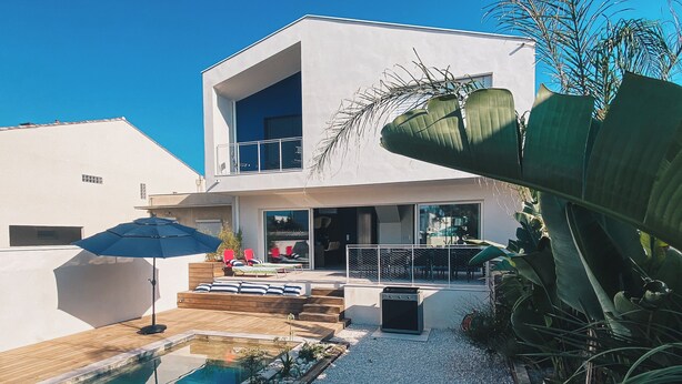 Una casa moderna de dos pisos con piscina, mobiliario exterior y un área de patio.