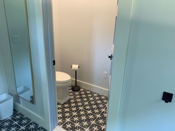 Un baño pequeño con un inodoro, un dispensador de papel higiénico y un piso con un diseño de baldosas geométricas.
