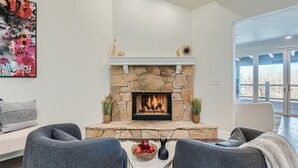 A modern living room with a stone fireplace, grey sofas, and a large window offering a view.