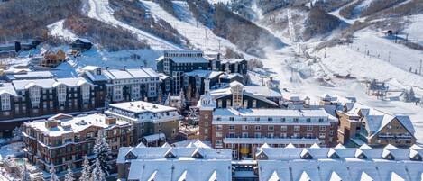 Un pueblo cubierto de nieve con varios edificios, incluyendo un hotel de estilo arquitectónico particular y una pista de esquí al fondo.