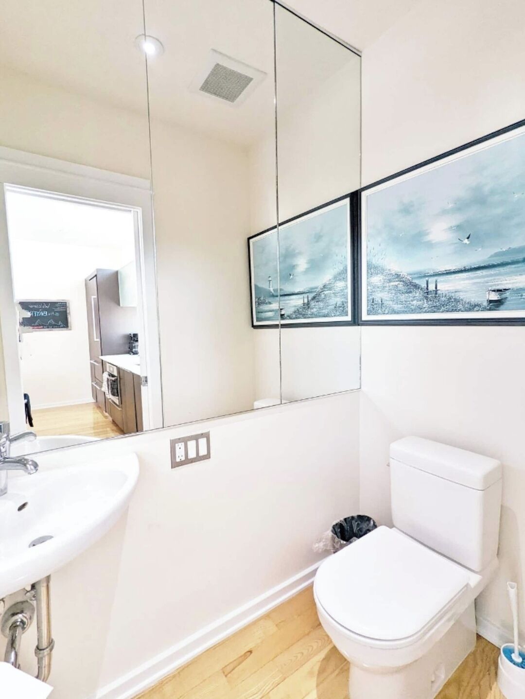 Ein modernes Badezimmer mit Waschbecken, Toilette und großem Spiegel. Zwei gerahmte Bilder hängen an der Wand.