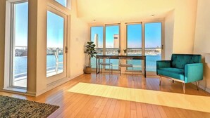 Un salon spacieux avec de grandes fenêtres, un fauteuil de couleur turquoise et un plancher en bois.