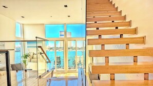 Un intérieur moderne avec un escalier en bois, de grandes fenêtres et une vue sur la mer.