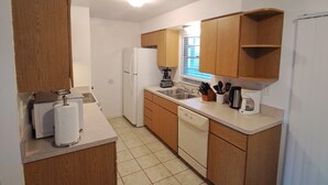A compact kitchen with wooden cabinets, a white refrigerator, a dishwasher, and a coffee maker on the counter.