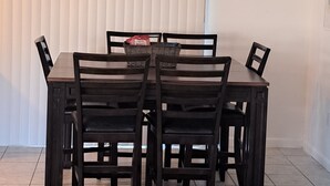 A dining area with a rectangular table and six chairs, a ceiling light fixture, and a window with blinds.