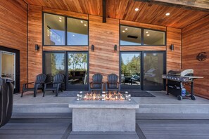 Un patio extérieur moderne doté d’un foyer, de sièges et d’un chariot-barbecue.
