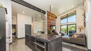A modern kitchen with a central island, built-in oven, and a large window overlooking a balcony. - Custom modern home near Olympic National Park (Port Angeles)