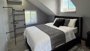 Un dormitorio con techo inclinado, una cama con cabecera, un perchero y una ventana con persianas.