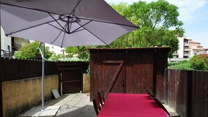 A patio area with a table and chairs under a large umbrella, a wooden shed, and a wooden fence. - Appart. T3 au Port de Capbreton, Espace Piétonnier, 800m Plage et Centre Ville (Capbreton)