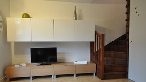 A modern living room with a flat-screen TV on a wooden console, white cabinets above, and a wooden staircase to the right. - Appart. T3 au Port de Capbreton, Espace Piétonnier, 800m Plage et Centre Ville (Capbreton)