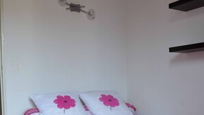 A bed with a striped pink and white bedspread, two pillows with pink floral designs, and a wooden floor. - Appart. T3 au Port de Capbreton, Espace Piétonnier, 800m Plage et Centre Ville (Capbreton)
