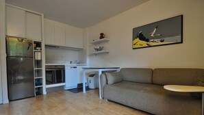 A modern kitchen with white cabinets, a built-in oven, and a stainless steel refrigerator. There is a grey sofa and a small table with a white tray in the living area. - Appart. T3 au Port de Capbreton, Espace Piétonnier, 800m Plage et Centre Ville (Capbreton)