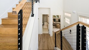 A staircase with wooden steps and black metal railings, leading to a room with a sofa and a window. - The Haven on Hibiscus (Greer)