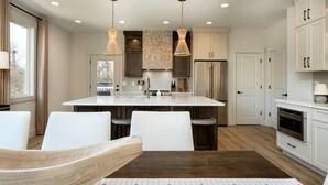 A modern kitchen with white cabinetry, a central island, and pendant lighting. - The Haven on Hibiscus (Greer)