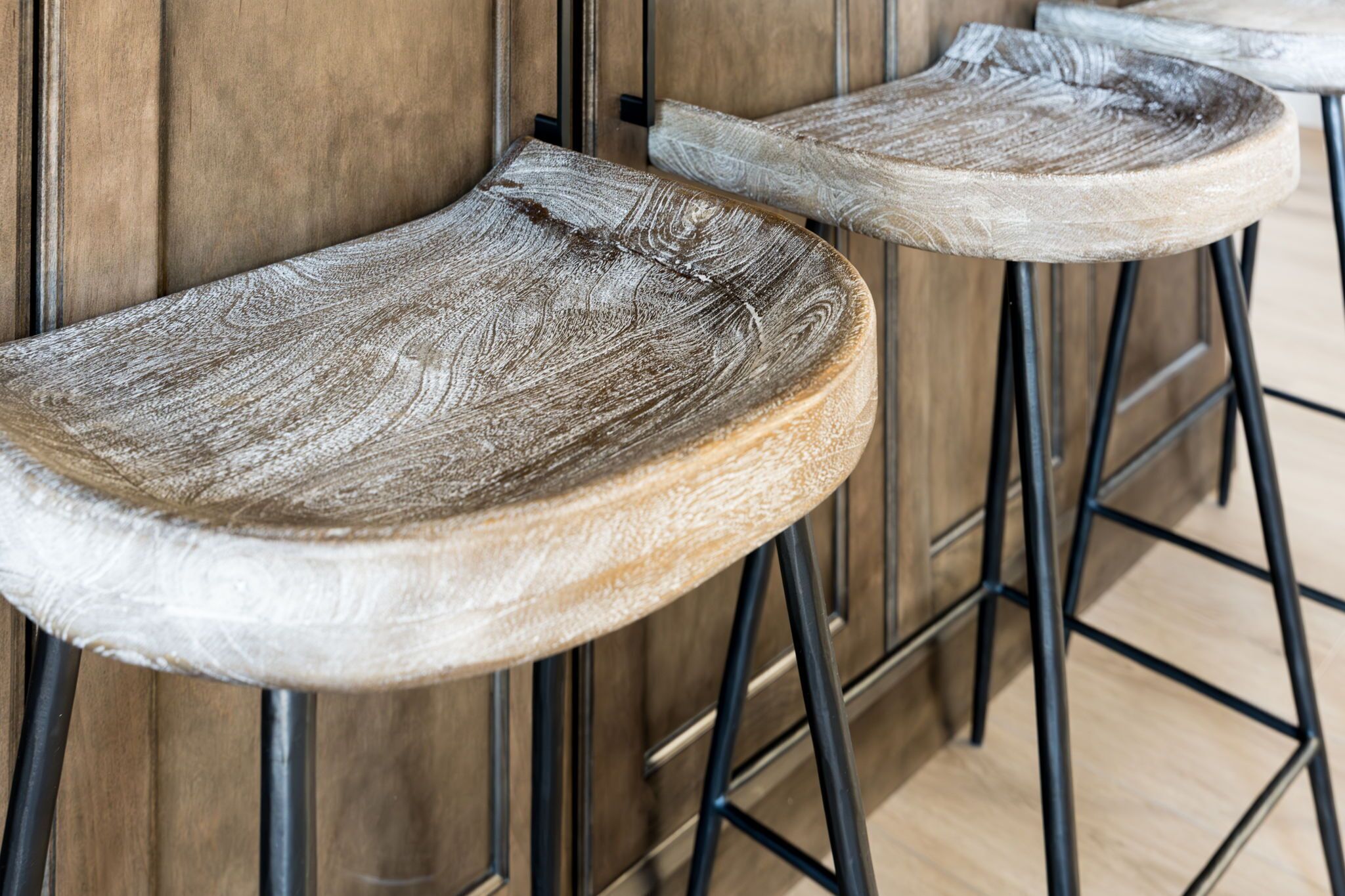 Two wooden bar stools with metal legs against a wooden wall.