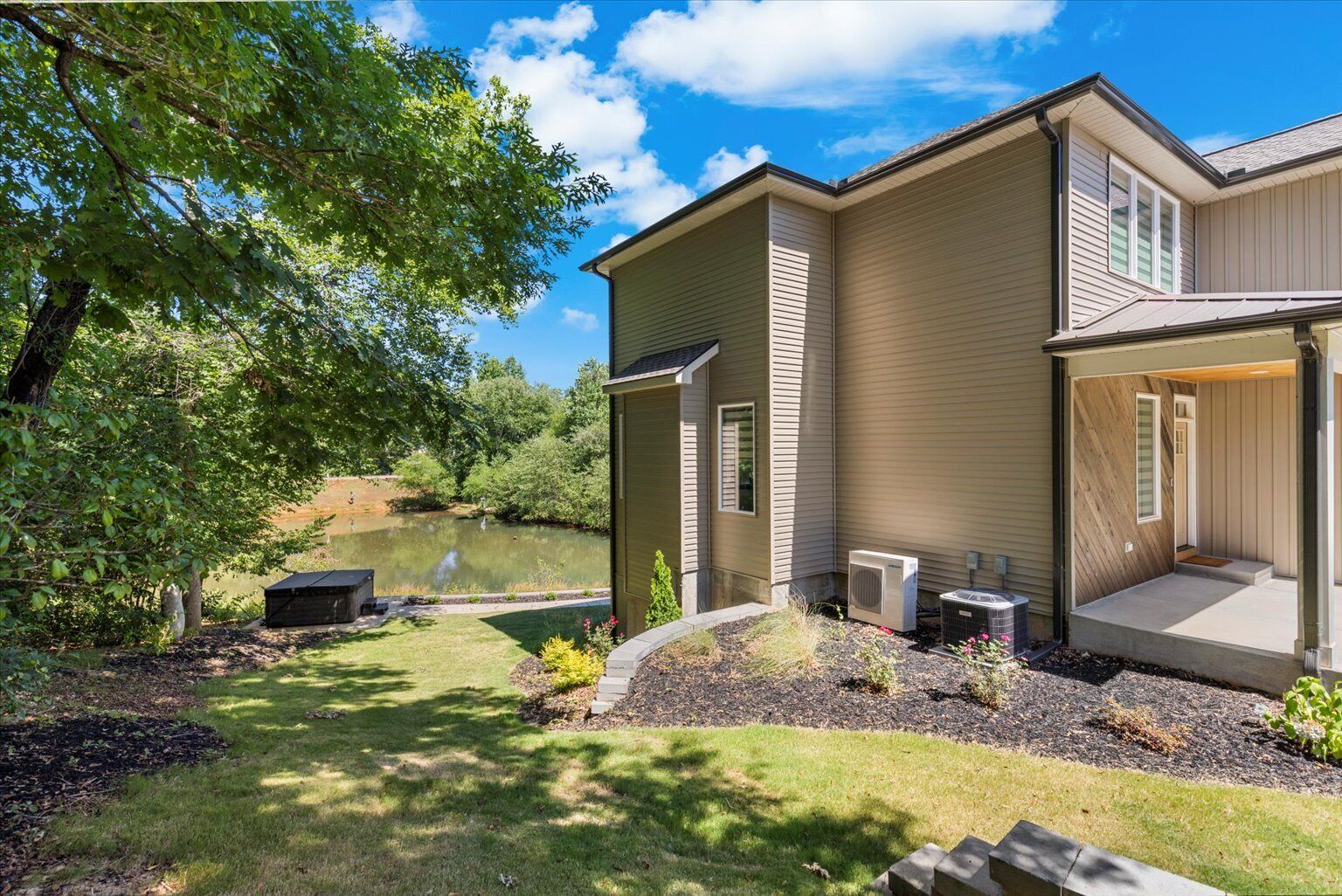 A two-story house with a pond, outdoor seating, and an air conditioning unit.