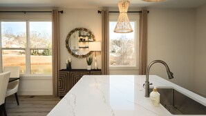A kitchen with a large island, a sink, and a dining area with chairs. - The Haven on Hibiscus (Greer)