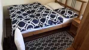 Ein Bett mit gemustertem Überwurf, einem hölzernen Kopfteil, einem Nachttisch mit einer Vase und einem Teppich mit Muster.