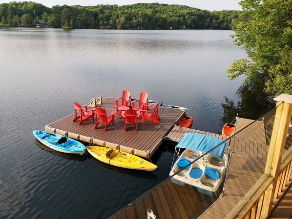 Une jetée en bois avec des chaises et des tables rouges, un petit bateau et un kayak.
