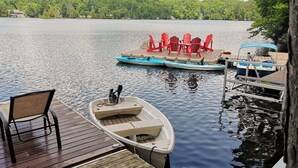 Ein Holzsteg mit einem Ruderboot und roten Stühlen an einem stillen See, umgeben von üppiger Vegetation.