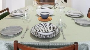 A dining table set with plates, glasses, and cutlery, with a view of a kitchen and a staircase in the background.