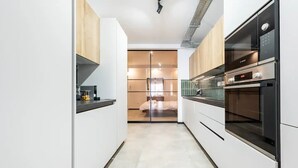 A modern kitchen with white cabinets, a Bosch oven, and a glass door leading to a bedroom.