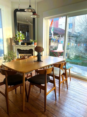 En matplats med ett träbord och stolar, en vas med blommor och utsikt över omgivningen genom ett stort fönster.