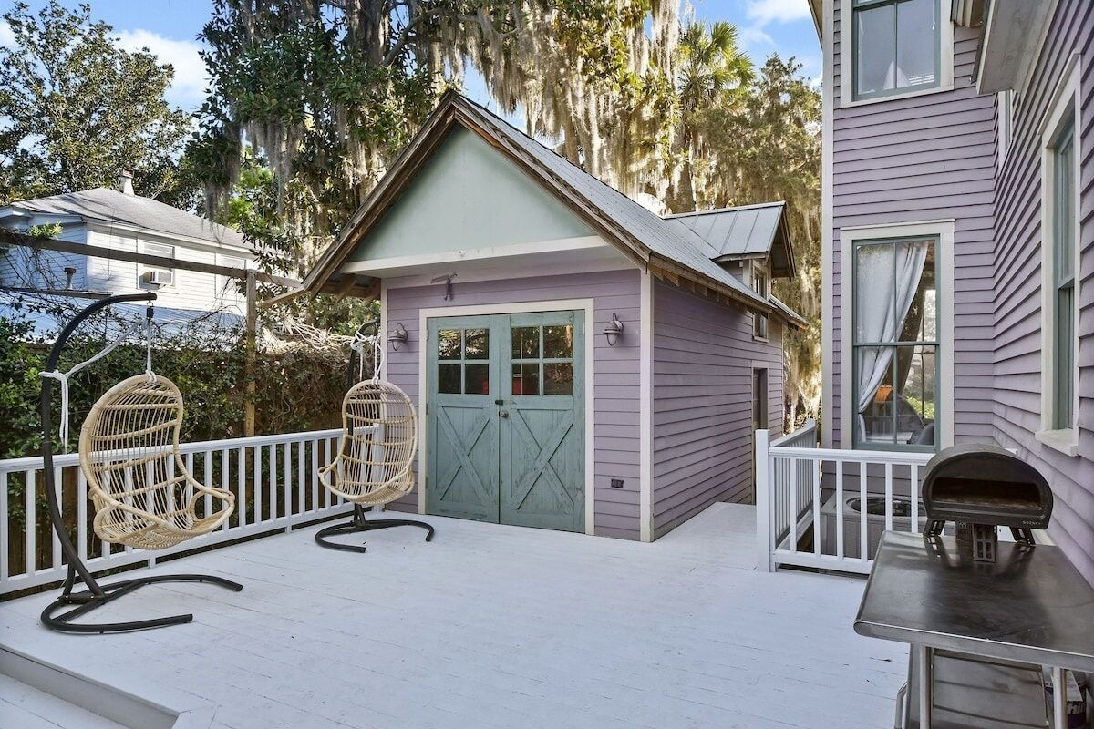 A small, single-story building with a porch, two wicker chairs, and a grill.