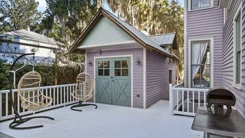 A small, single-story building with a porch, two wicker chairs, and a grill.