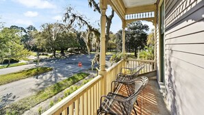 A porch with two wicker chairs, a stop sign, and a street view with trees and a parking lot.