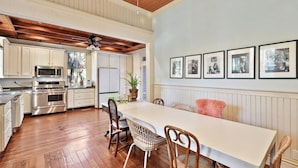 A spacious kitchen with wooden floors, white cabinetry, and a dining area with wicker chairs and a white table.