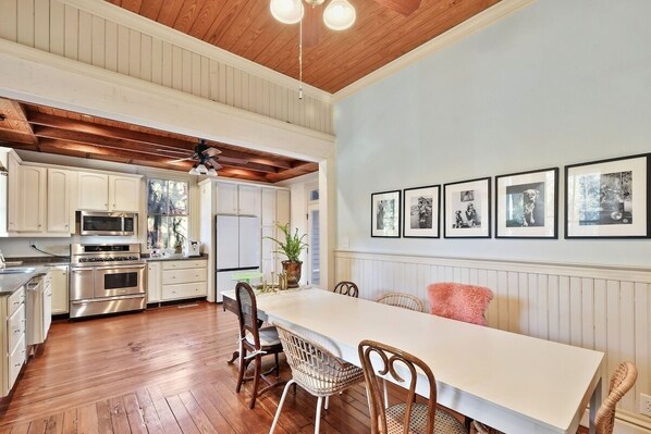 A spacious kitchen with wooden floors, white cabinetry, and a dining area with wicker chairs and a white table.
