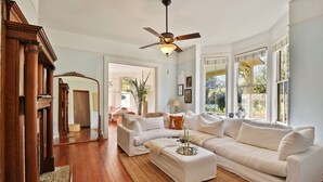 A spacious living room with a large white sectional sofa, a wooden floor, and a ceiling fan.