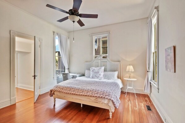 A bedroom with a bed, a ceiling fan, a nightstand, a lamp, and a window.