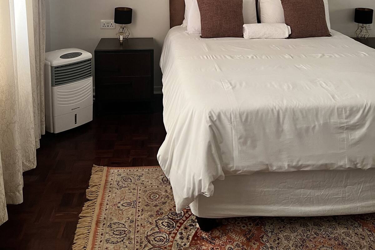 A bedroom with a large bed, bedside tables, a heater, and decorative wall mirrors.