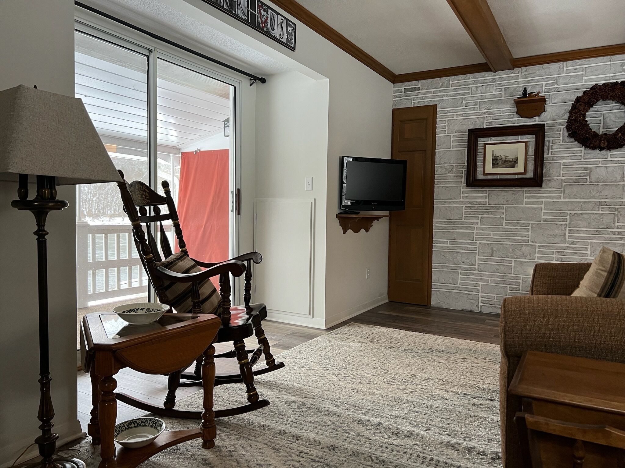 A living room with a rocking chair, a television mounted on the wall, a fireplace, and a stone-textured wall.