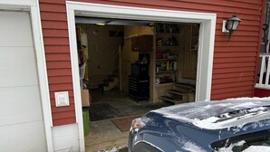 A garage with a car covered in snow, a ladder, and shelves stocked with various items. - Allegheny River House (Tidioute)