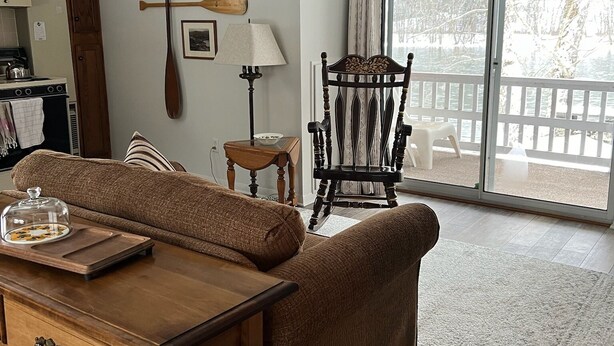 A cozy living room with a wooden sofa, a dining table, and a view of a snowy landscape through large sliding glass doors. - Allegheny River House (Tidioute)