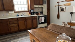 A kitchen with wooden cabinets, a stove, and a dining area with a table and a sofa. - Allegheny River House (Tidioute)