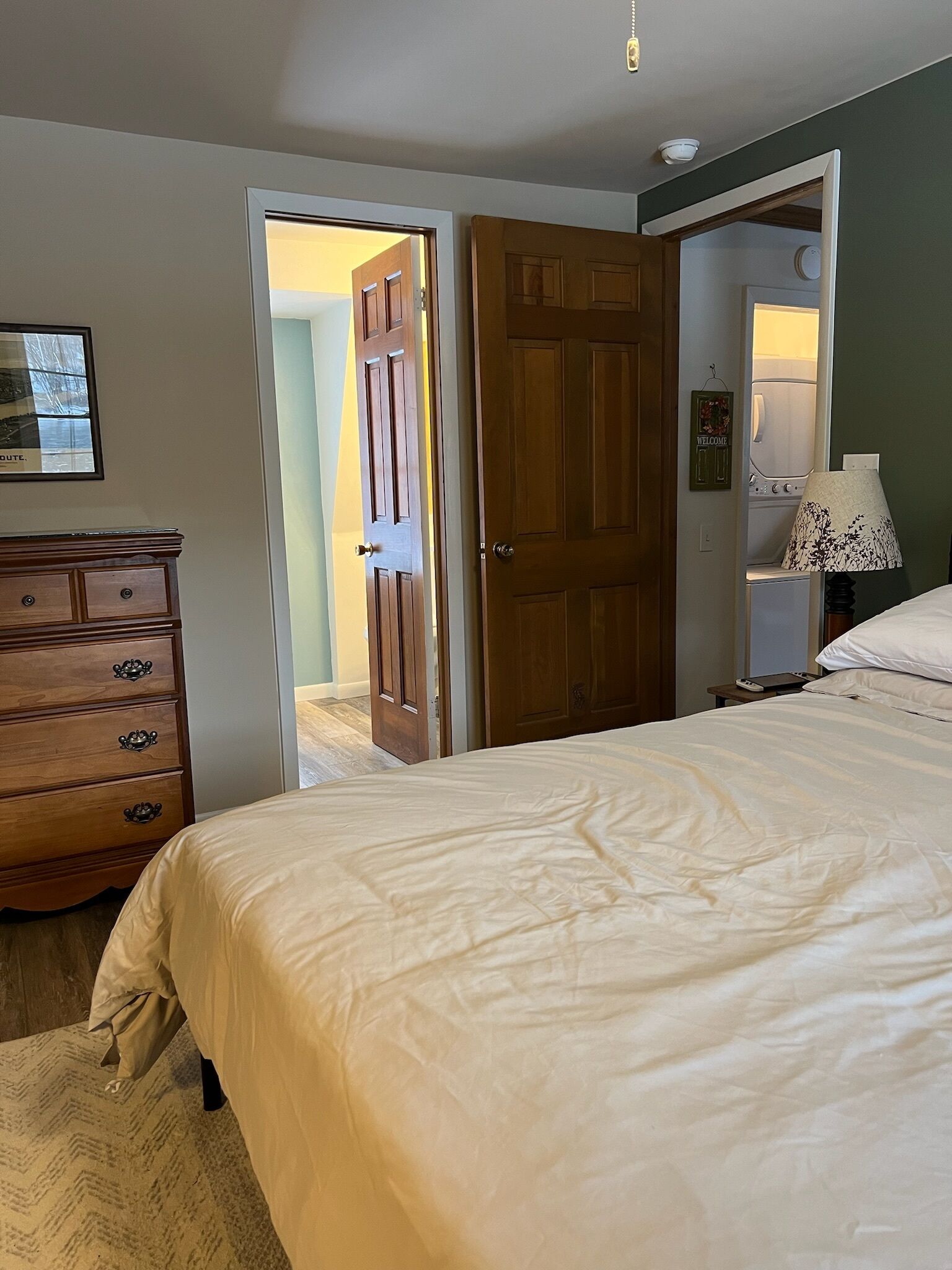 A bedroom with a bed, dresser, and a door leading to another room.
