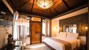 Ein Schlafzimmer mit einem hölzernen Bett, einer Chandelierleuchtre und einer Buddha-Statue.