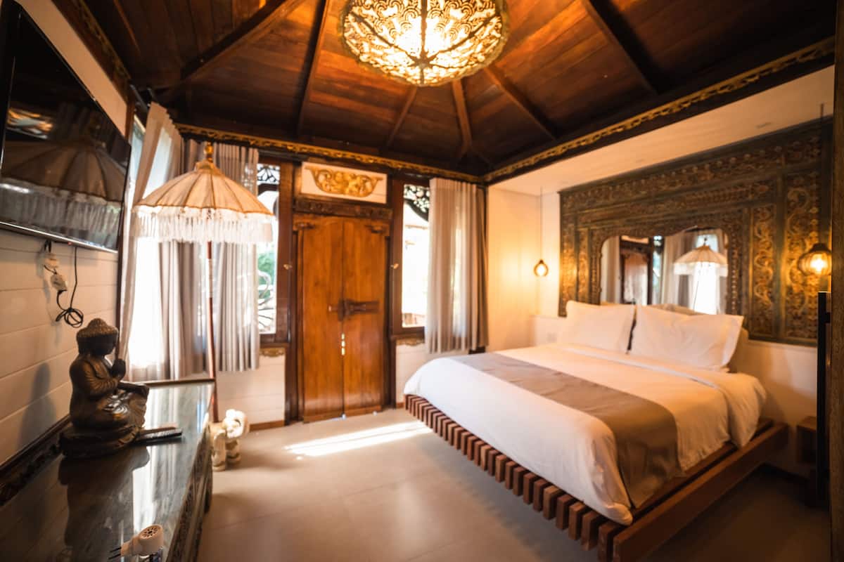 A bedroom with a wooden bed, a chandelier, and a Buddha statue.