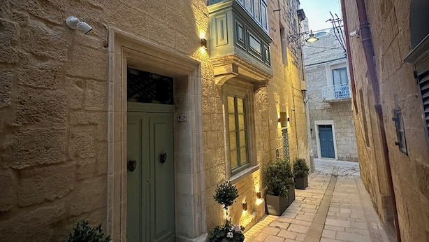 A narrow alleyway with stone buildings, a green door, and potted plants. - Casa Norte (Birgu)