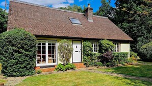 A single-story house with a tiled roof, a front door, and a small garden area with a lawn and a few shrubs. - Picturesque 5 Bed Cottage Lingfield, Surrey (Newchapel)