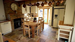 A kitchen with a brick fireplace, wooden dining table, and hanging copper pots. - Picturesque 5 Bed Cottage Lingfield, Surrey (Newchapel)