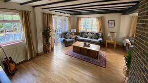 A cozy living room with wooden flooring, a sofa set, a coffee table, and a guitar. - Picturesque 5 Bed Cottage Lingfield, Surrey (Newchapel)