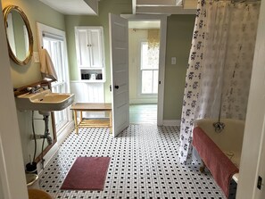 Un baño con lavamanos, espejo y retrete. Hay un taburete de madera y una alfombra roja en el suelo.